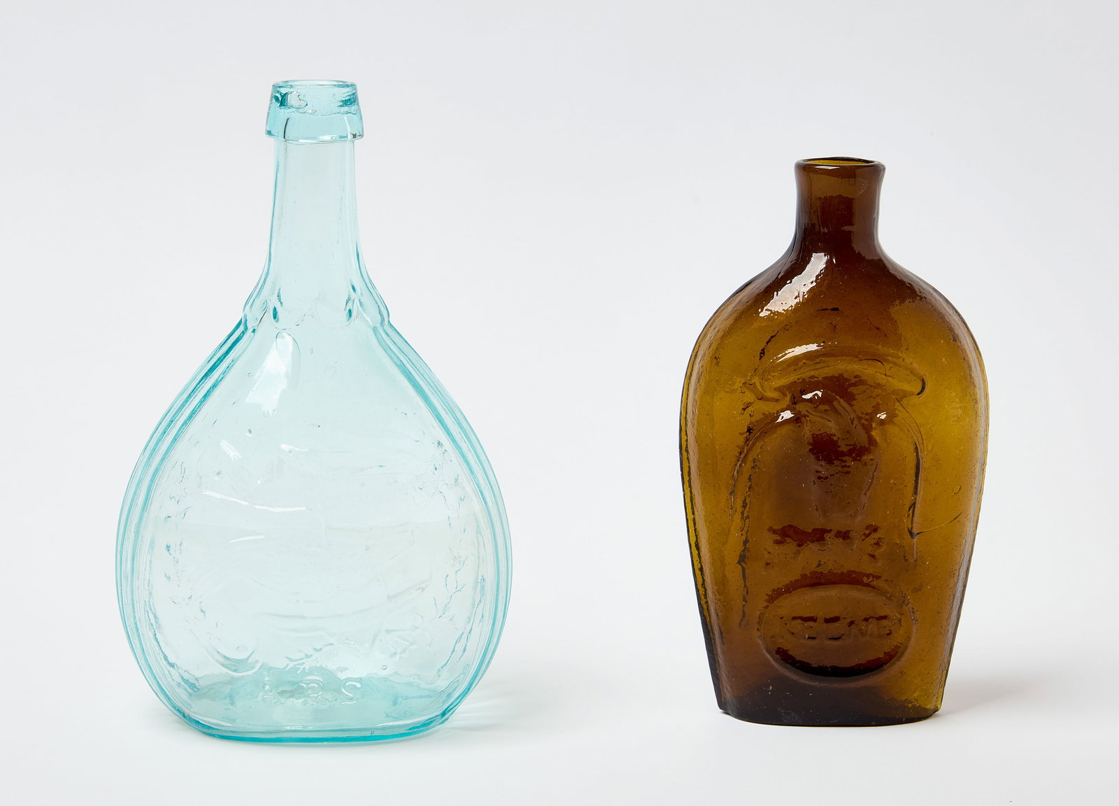 Two Masonic Flasks: Two Masonic flasks. Embossed glass with pontil base. One in light blue with clasped hands, 'union' below, the masonic compass and square. Reverse side depicts bird with shield and the ini