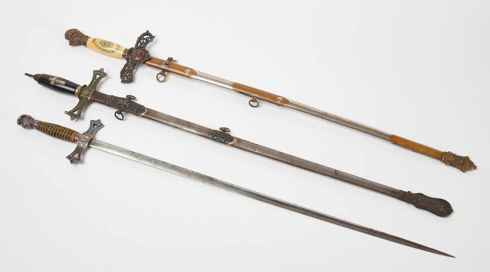 Three Masonic Swords: Three Masonic swords. First is a W. Clauberg in the Solingen style with metal sheath. Second is an intricate Knights Templar sword with bone-grip and metal sheath. Third is Horstmann Philadelphia swor
