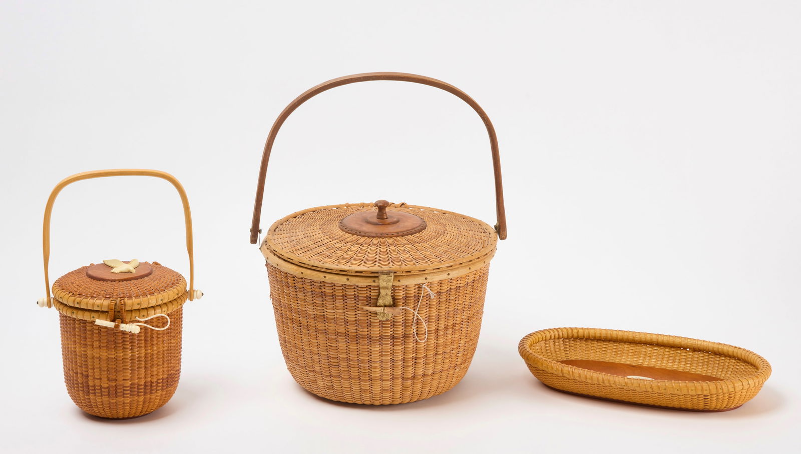 Three Nantucket Baskets: Three Nantucket baskets. A tray dated 1992 and signed William Reese. A large handled covered sewing basket and a purse basket with carved bone bird. Tray: H 2in. L 12-1/4 in W 7-1/4 in. Signed. Sewing