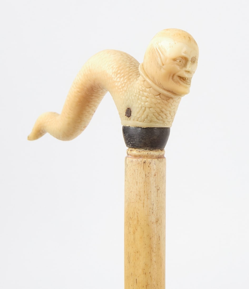 Scrimshaw Walking Stick with Carved Sea Creature: Scrimshaw walking stick with sea creature. Carved bone handle with a human face and serpent body. Whale bone shaft with ebony spacer. American, mid to late 19th century. Provenance: Collection of Sall