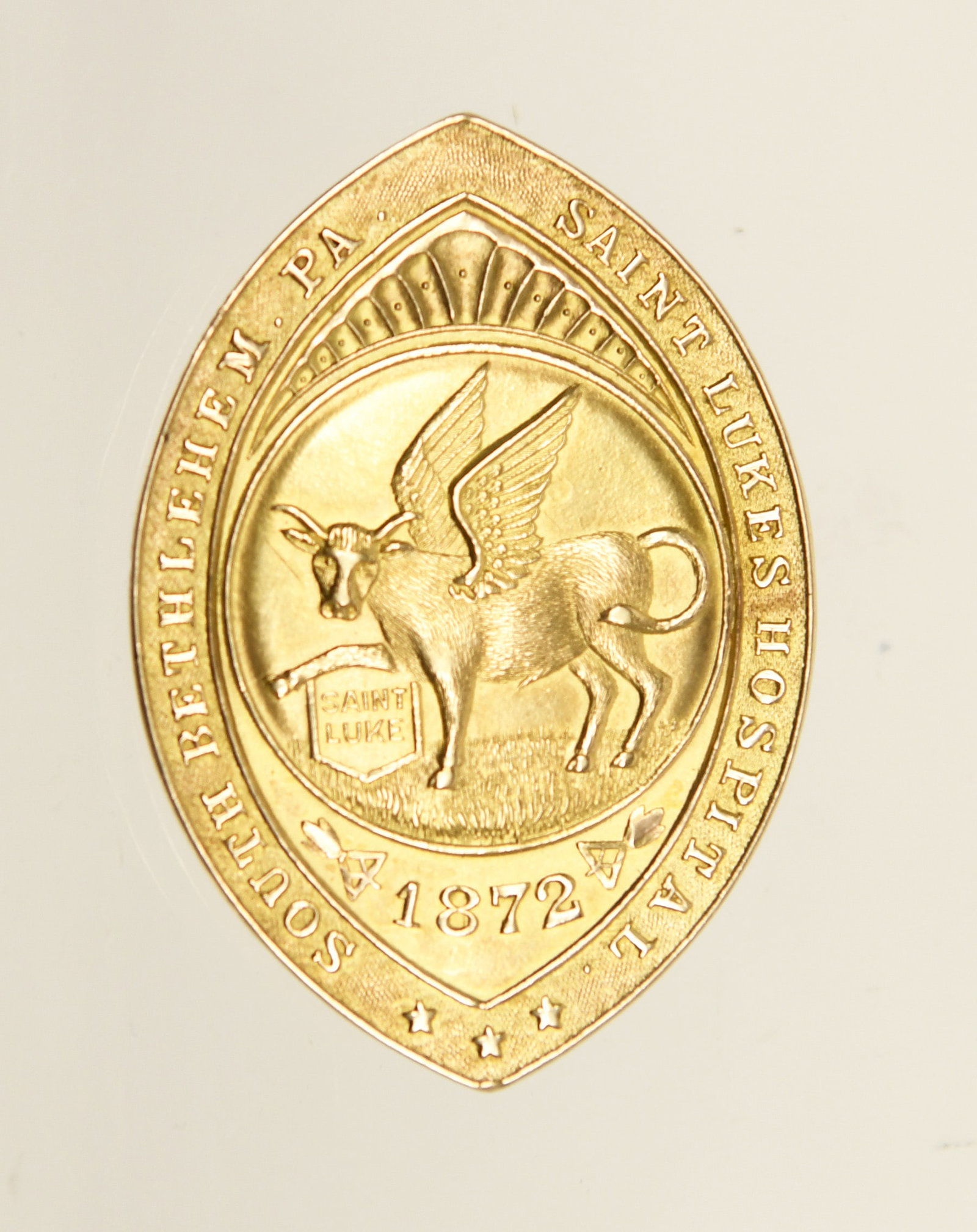14k Gold Saint Luke's Hospital Badge: 14 gold Saint Luke's Hospital badge inscribed to Hazel May Wagner and dated 1915. Front emblem shows a date of 1872 and a winged ox.7.4 dwt.L 2 in. W 1-3/8 in.
