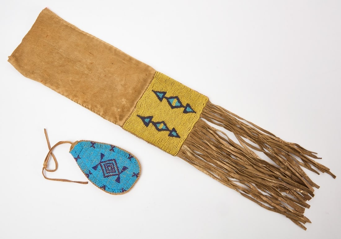 Two Beaded Native Bags: Two Native beaded bags. A beaded hide and fabric pipe bag, together with a small beaded pouch on hide with blue beads. Both are sinew sewn.Pipebag: L with fringe: 27 in.Pouch: L 5-1/2 in.