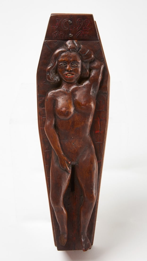 Folk Art Coin Bank - Lady on Coffin: Folk art erotic coin bank depicting a nude woman laying on top of a coffin. Coin slot betweenher legs. Carved, varnished and painted wood. American, circa 1920.L 13-1/4 in. W 4-1/2 in. D 3-1/2 in.