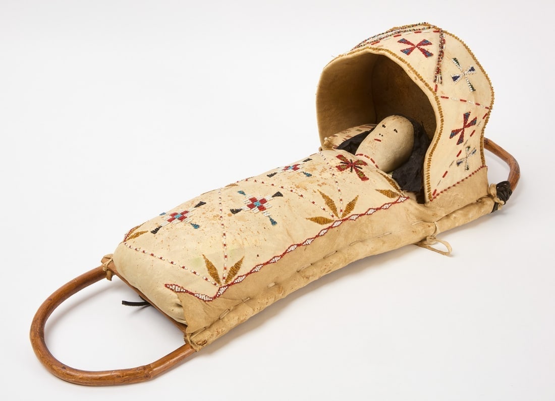 Native American Cradleboard with Doll: Apache cradleboard with doll. Beaded decoration on hide. Circa 1920.H 30 in. W 10-1/4 in.