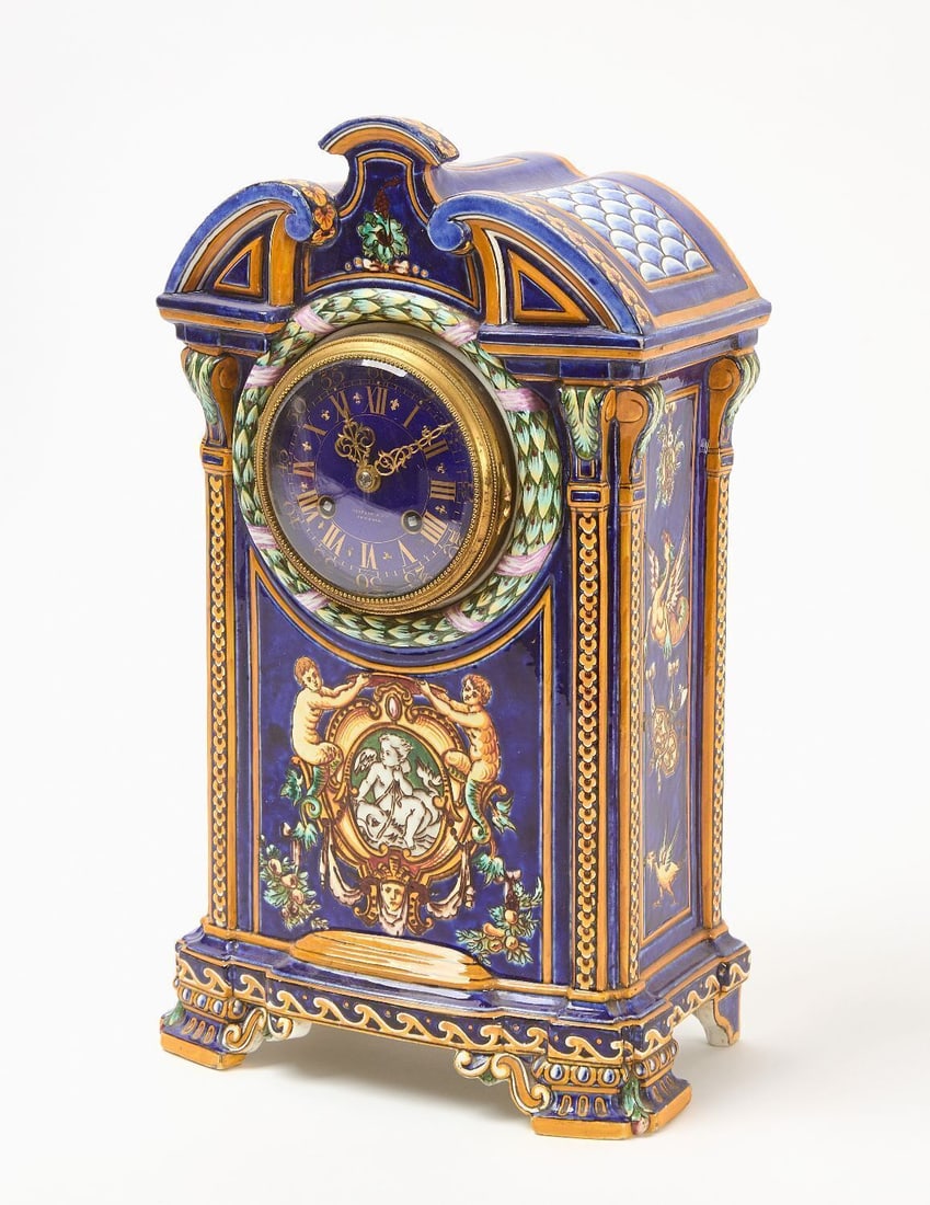 Tiffany & Co. Majolica Shelf Clock: Tiffany & Co. Majolica shelf clock. Porcelain with motifs of cherubs and mystical creatures. Includes pendulum and key. H 15-1/4 in. W 9 in. D 5 in.