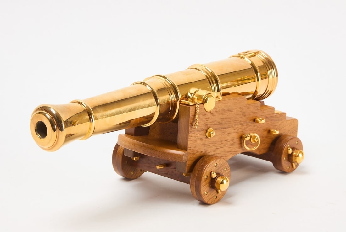Brass Cannon Model: Model of a cannon. Brass and wood. Lucite showcase included as shown. Case: H 7-3/4 in. W 17 in. D 9 in. Cannon: H 4-1/2 in. W 5 in. L 11-7/8 in.