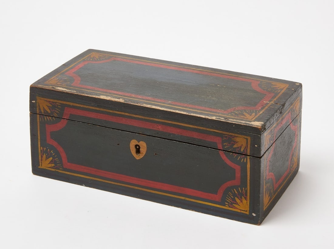 Miniature Painted Box: A 19th century miniature painted pine box with hinged lid and lock with key. The box is painted green with red, yellow, and black line borders and floral rays at each corner. H 4 in. W 10-1/4 in