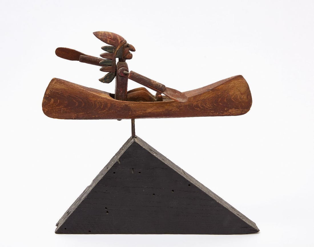 Folk Art Native American in Canoe Whirligig: Folk art whirligig depicting a native american in headdress paddling in a canoe. Mounted to black painted triangular wooden base. America, circa 1920. Overall: H 11-1/4 in. L 11-1/2 in. 