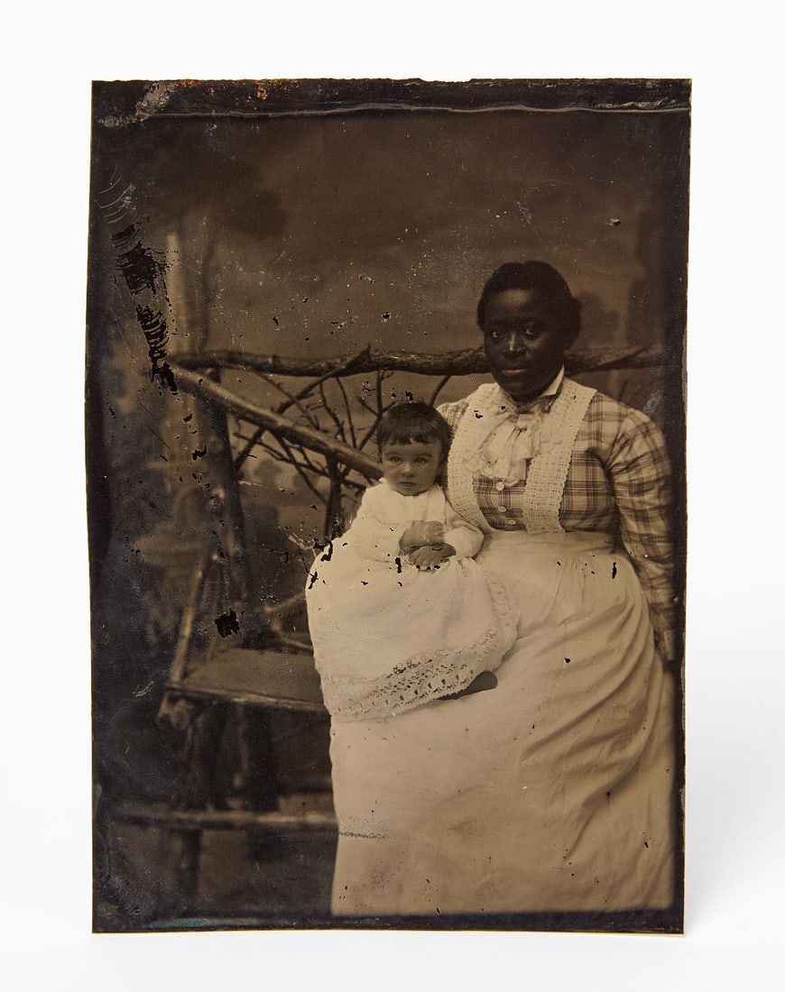 Tintype of a Black Nanny and Infant: 1/4 plate tintype of a Black care-giver or nanny with her charge, a young white child. Period, likely non-original frame. American, circa 1870. Frame: H 7 in. W 6 in. Image: H 4-7/8 in. W 3-1/2 