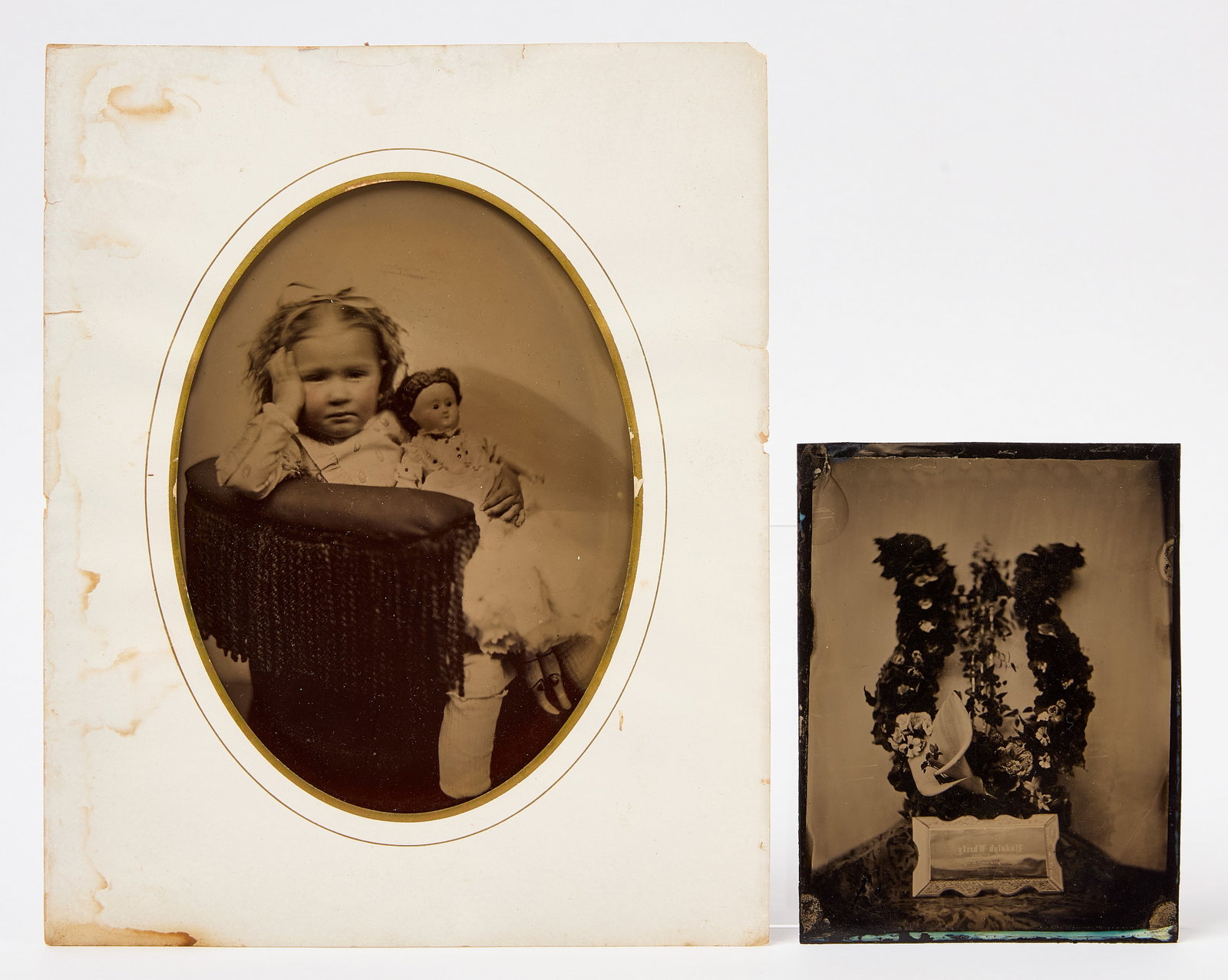 Two Large Tintypes - Girl with Doll, and Memorial Wreath: Two large tintype photographs. Full plate tintype of a seated girl holding a large china-head doll. Together with a half plate tintype of a memorial lyre form wreath of flowers and a casket plaque. Am