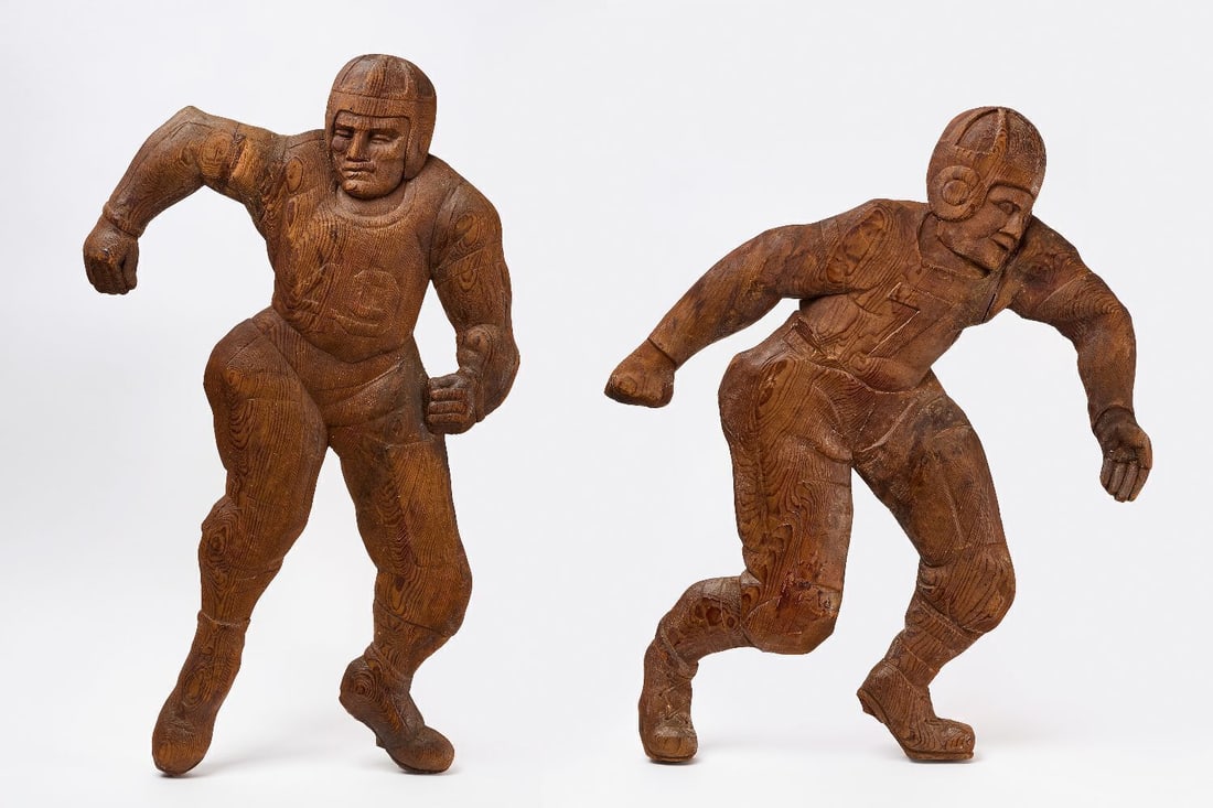 Pair of Carved Wood Football Player Athletic Store Displays: Monumental pair of football player store displays. Carved wood. Purportedly from an athletic supply store. American, circa 1930. H 37 in. W 23 in. and H 32 in. W 27-1/2 in.