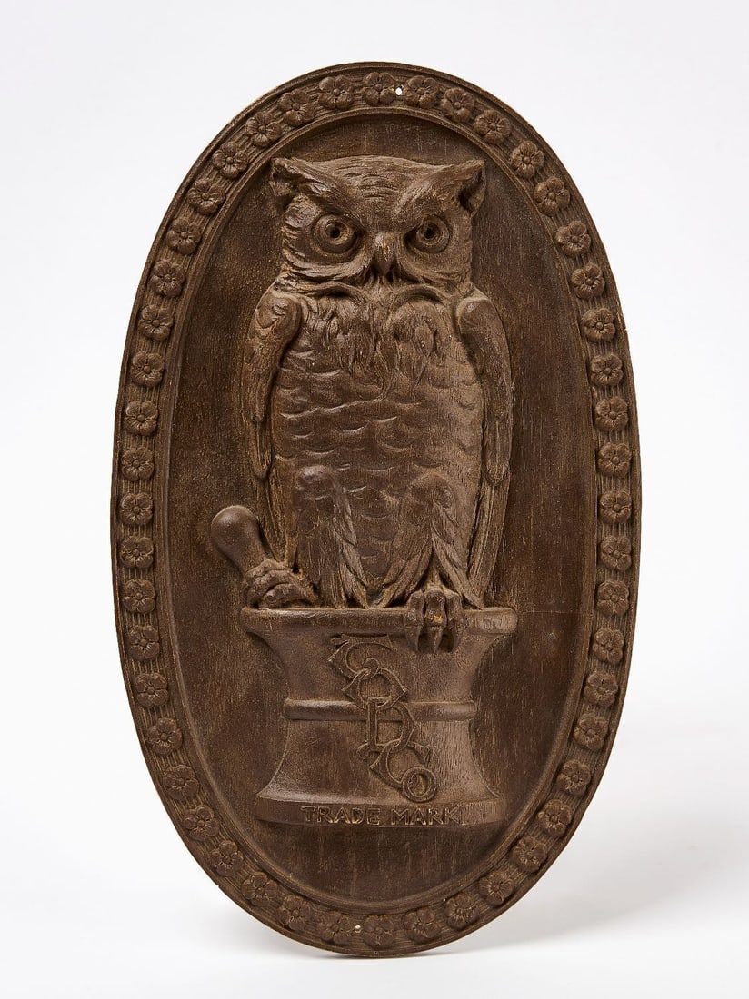 Owl Drugs Trade Sign: Owl Drugs trade sign. Depicts a graphic of an owl on top of a mortar and pestle. Oval border of flowers or rosettes. Composite material. American, circa 1920. H 15-1/2 in. W 9-1/4 in.