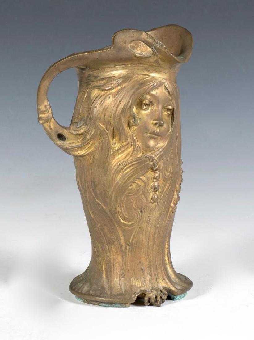 Georges Flamand Art Nouveau Bronze Ewer: Georges Flamand (French 1895-1925) Cast in the form of a young woman's face with flowing hair and Lily of the Valley, signed G. Flamand. 8.75 in. h. x 4 in.w. Condition: Filled fitting hole