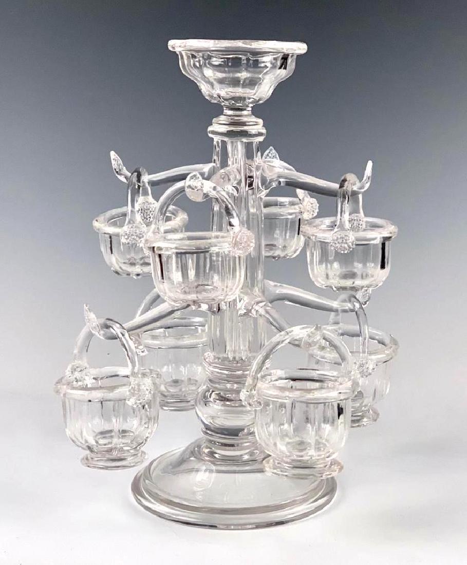 A Blown Glass Epergne: Faceted standard on circular foot, with eight applied scrolled arms supporting blown glass baskets with applied handles fastened by prunts. 13 in.h. Condition: Good