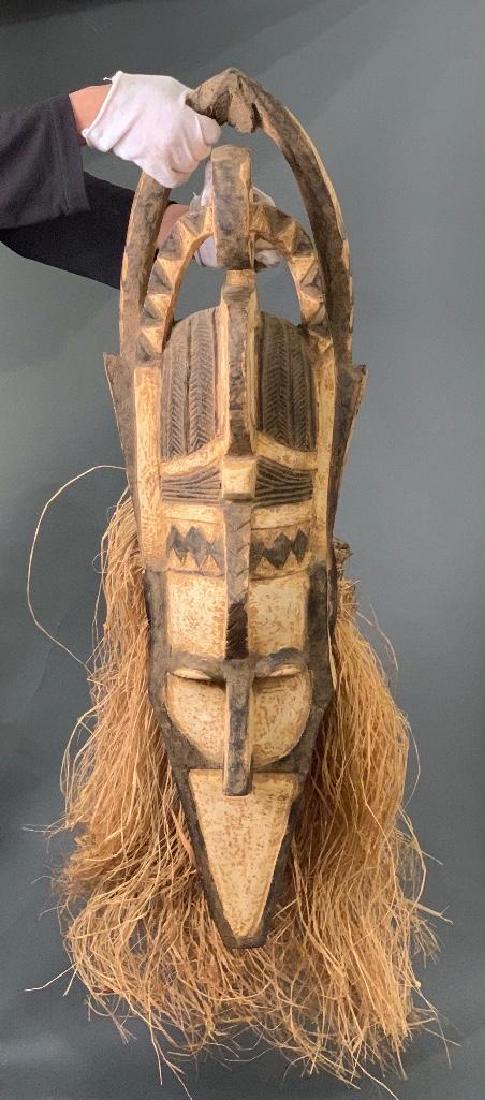 Banda Mask, Nalu People, Guinea: Elongated mask with white pigment, raffia decoration, crown, pointed chin and hooded eyes. 38.5"T. Appearing in harvest ceremonies, these mask are symbolic and are used for protection. Condition: good