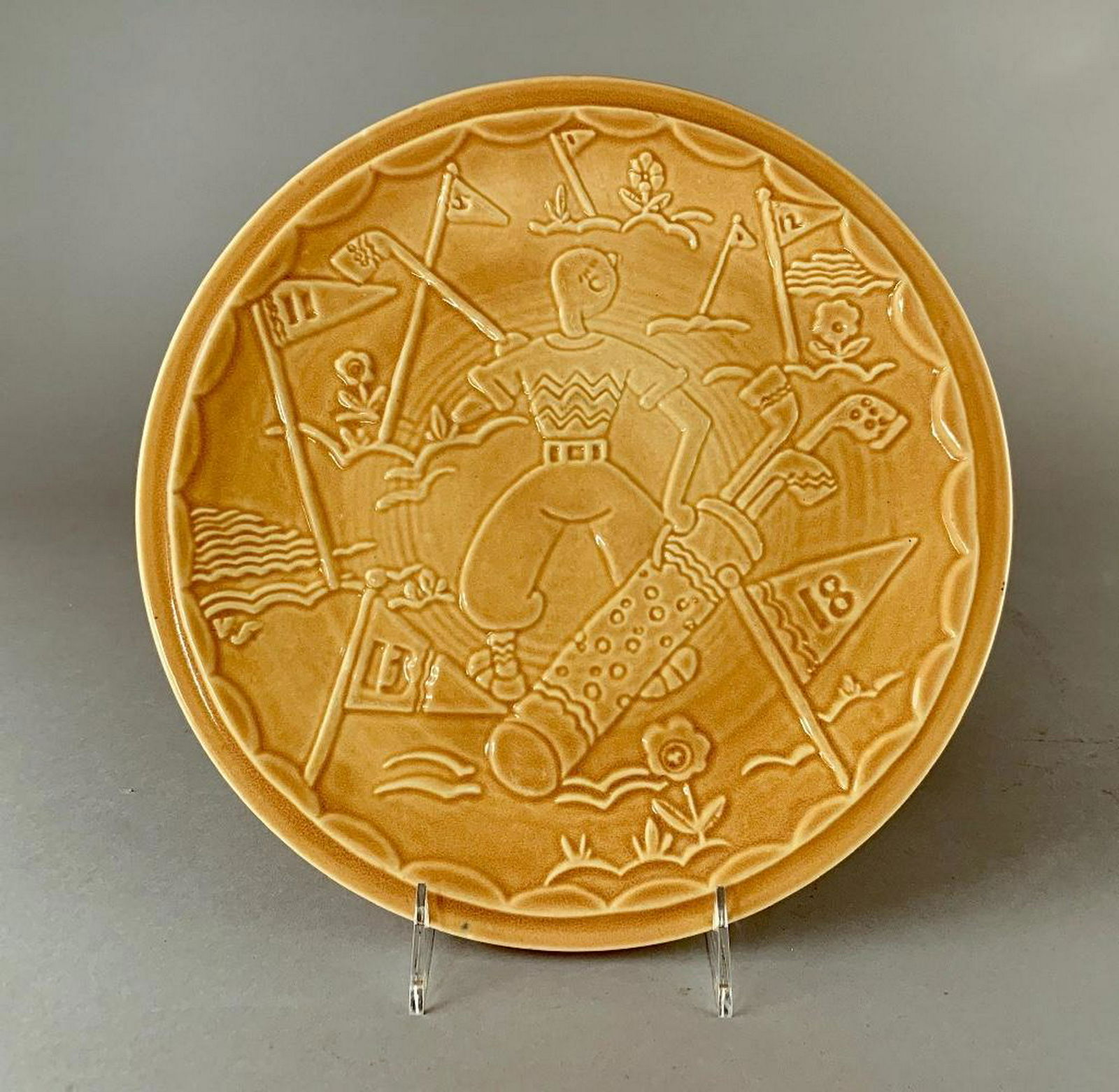 Viktor Schreckengost Rare Monochrome Glaze Golf Plate: Viktor Schreckengost (American, Cleveland School 1906-2008) for Cowan Pottery, Golf Plate, molded with a cheerful design of a golfer holding his bag of clubs with various pin flags and floral designs.