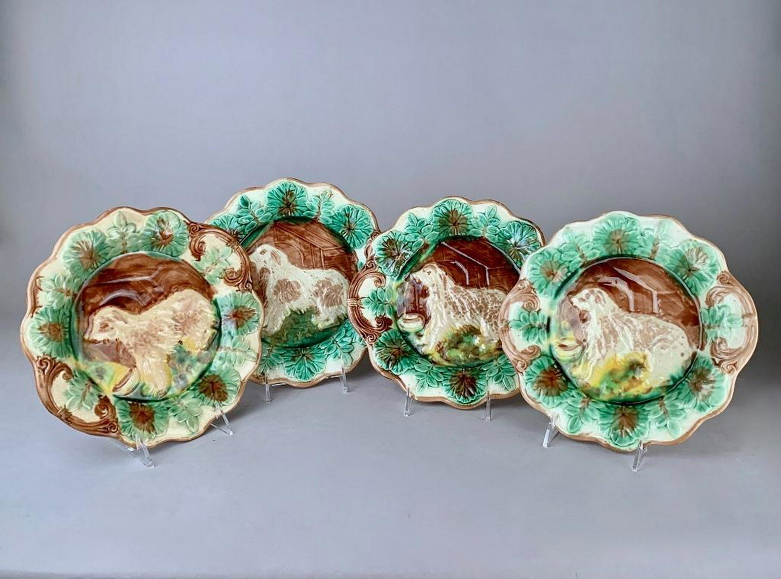 Four Majolica Dog Plates: Late 19th C., with scalloped rims, glazed in green and brown and molded with variously glazed dogs seated in front of dog houses. With sponge glazed design verso. 10.5 in. dia. Condition: One plate wi