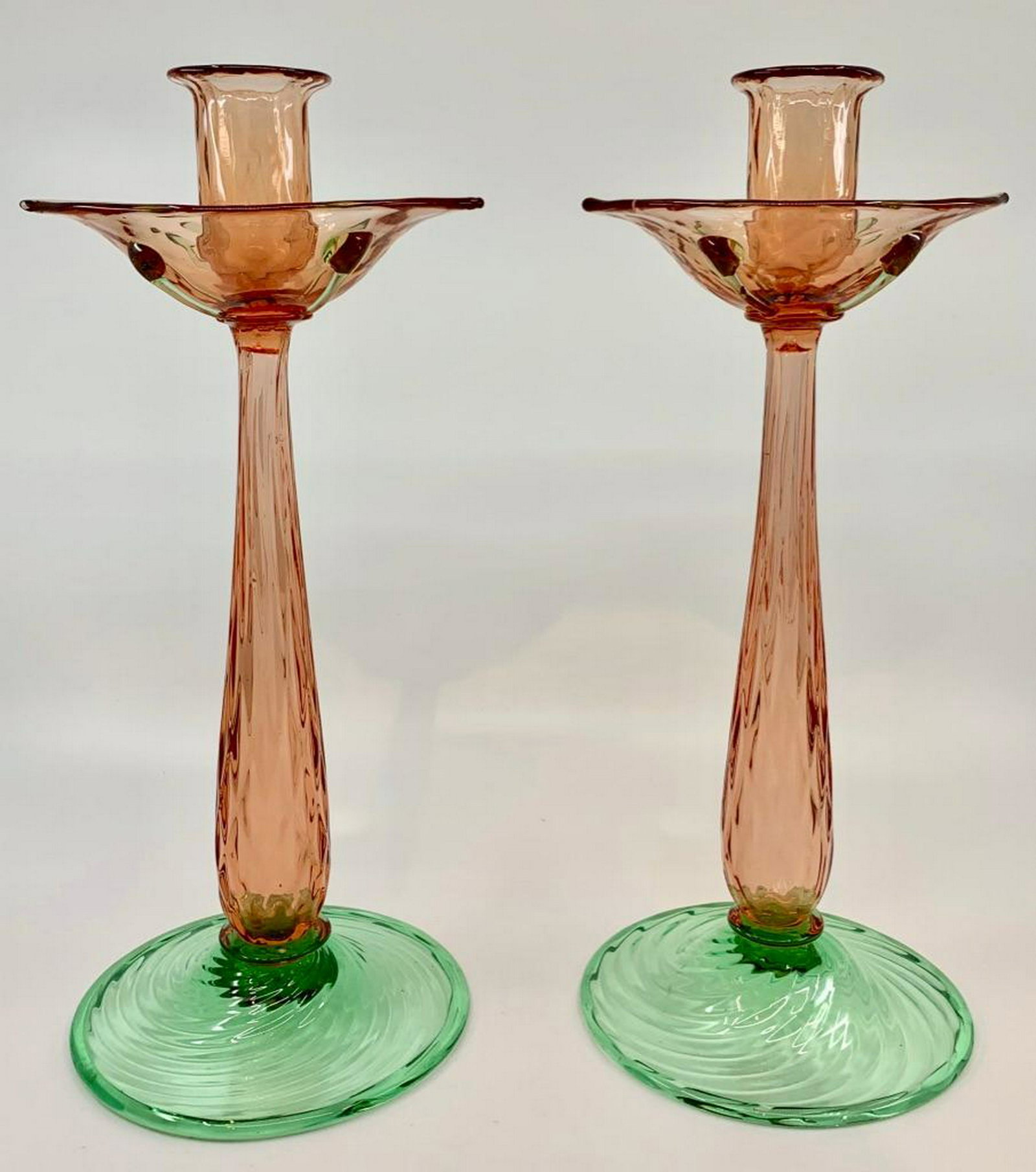 Steuben Pair of Pink and Green Blown Glass Candlesticks: Baluster standard in pink on wide green fluted circular foot, with quilted pattern drip pan and bobeche in pink, the underside of the drip pan applied with green trailed applications. 12.25 in.h. Cond