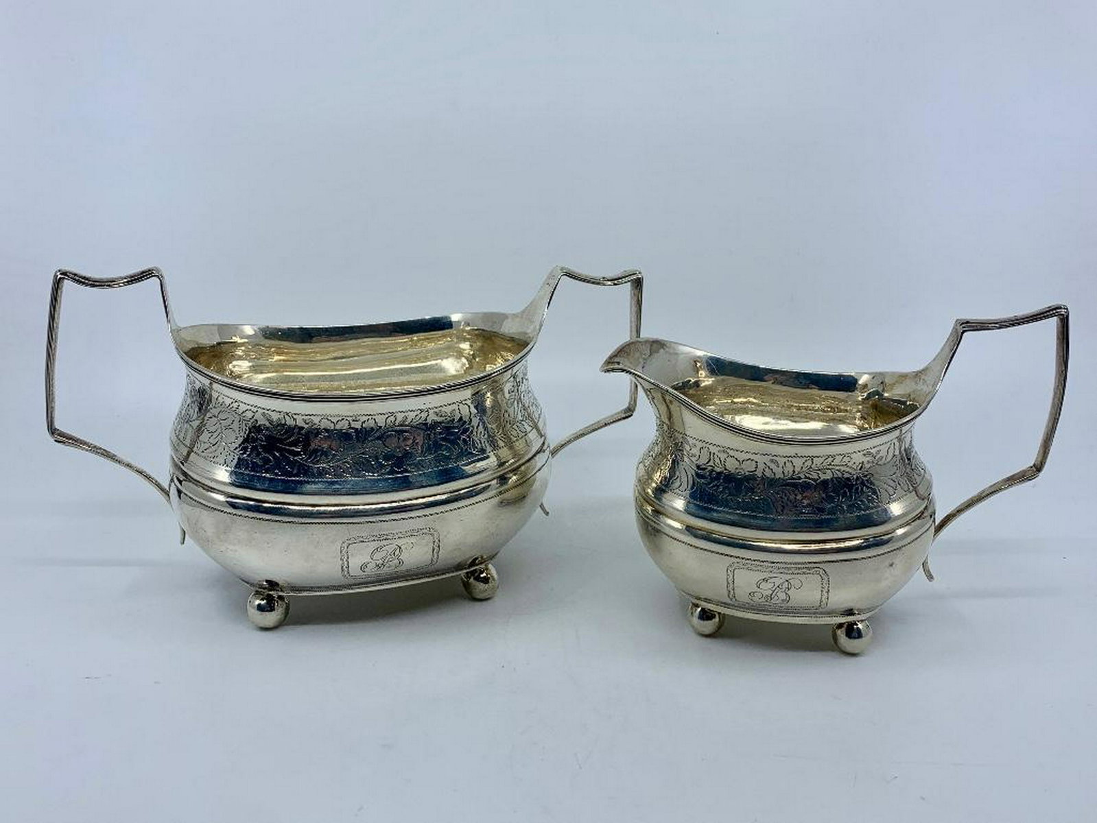 English Silver Sugar and Creamer, London, 1809: With maker's marks for Thomas Wallis and Jonathan Hayne, squared oval form on spherical feet, engraved around the shoulder with floral sprigs, monogrammed initial B. 14.40 oz. troy 4.5 x 8 x 4 in. Con