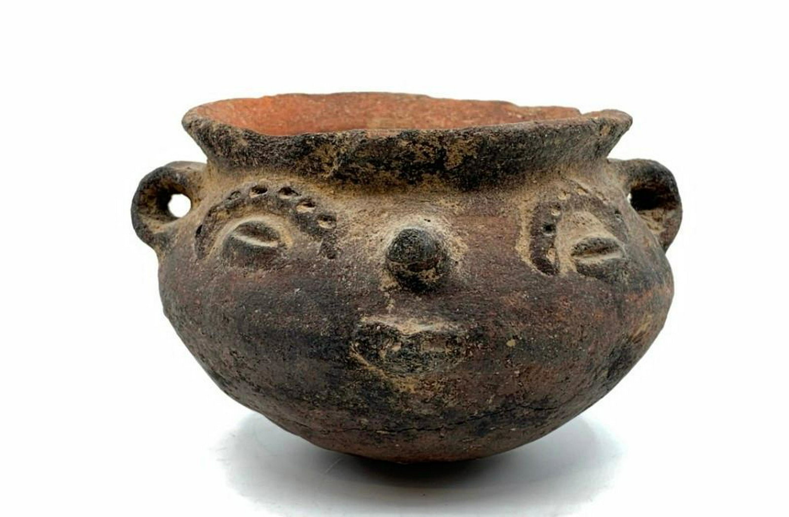 Pre-Colombian Face Mask Jar: Rounded form with rounded bottom and everted rim with applied ear ring handles, modeled with a face on both sides of the vessel. 3.25 in.h. x 5 in. w. Condition: Old breaks and losses commensurate wit