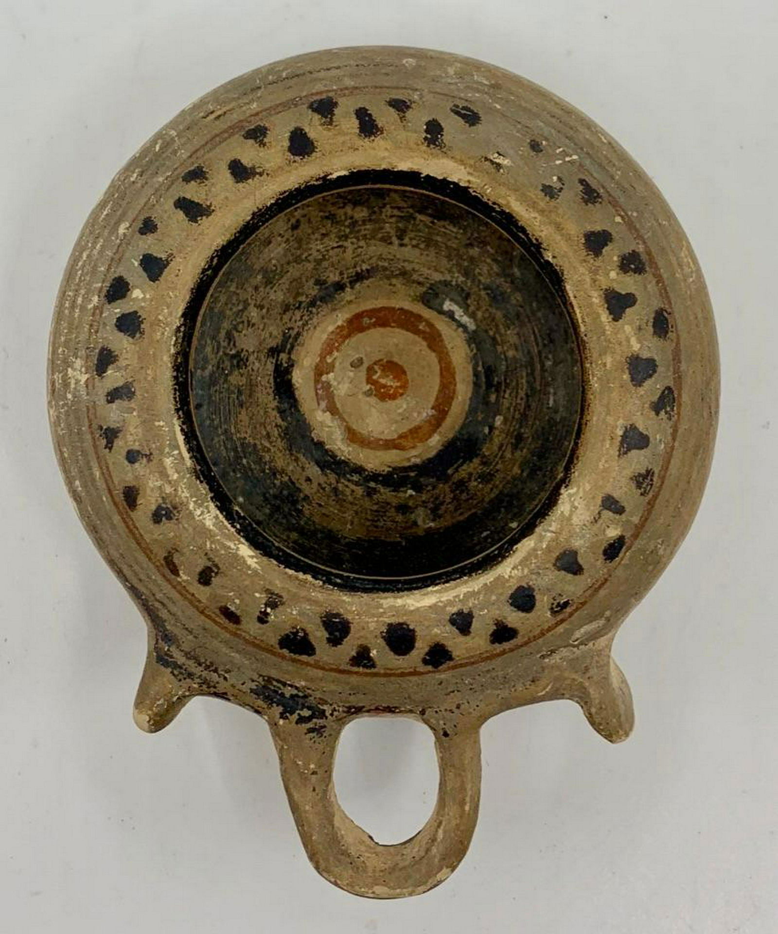 South Italian Antique Pottery Oil Lamp, c.4th c. BC: Circular form in buff pottery with applied loop handle and painted decoration in iron red and black. 3.75 in. dia. Condition: Good with normal wear.