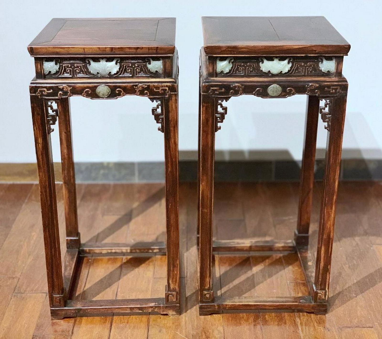 A Rare Pair of Chinese Carved Jade Mounted Plant Stands: 19TH CENTURY-Pair of carved wood stands, each with squared top over a frieze carved in relief with squared scrolls, inset with carved mutton fat jade masks, the lower part carved in relief with phoeni