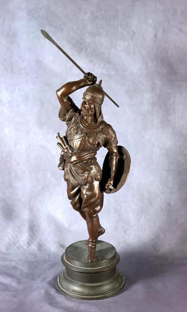 White Metal Figure of a Mercenary Soldier: Middle Eastern style armor with shield, daggers and lance, brown patination. 22.5 in. h. to top of spear. Condition: Good with minor wear to patination.