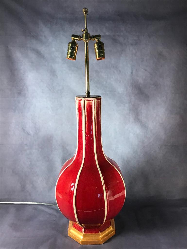 Chinese Oxblood Glaze Table Lamp: Sectioned form in oxblood glaze with pale celadon ribs, with gilt wood base and adjustable brass two light sockets. 21 in.h. to top of porcelain Condition: Very good.