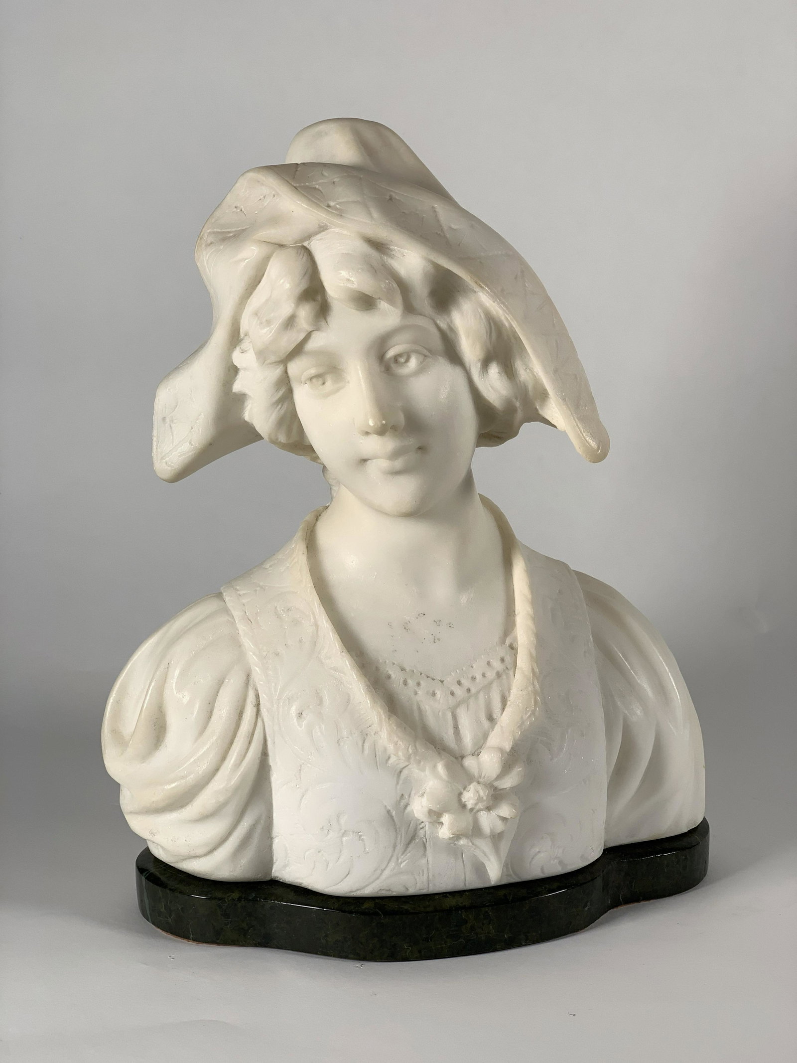Alabaster Bust of Young Woman with Hat: Alabaster Bust of Young Woman with Hat, early 20thc. with serene face looking slightly to right, with flower adorned dress, raised on conforming green marble base. 11 in. h x. 9 in. w. 4.5 in, d. Cond