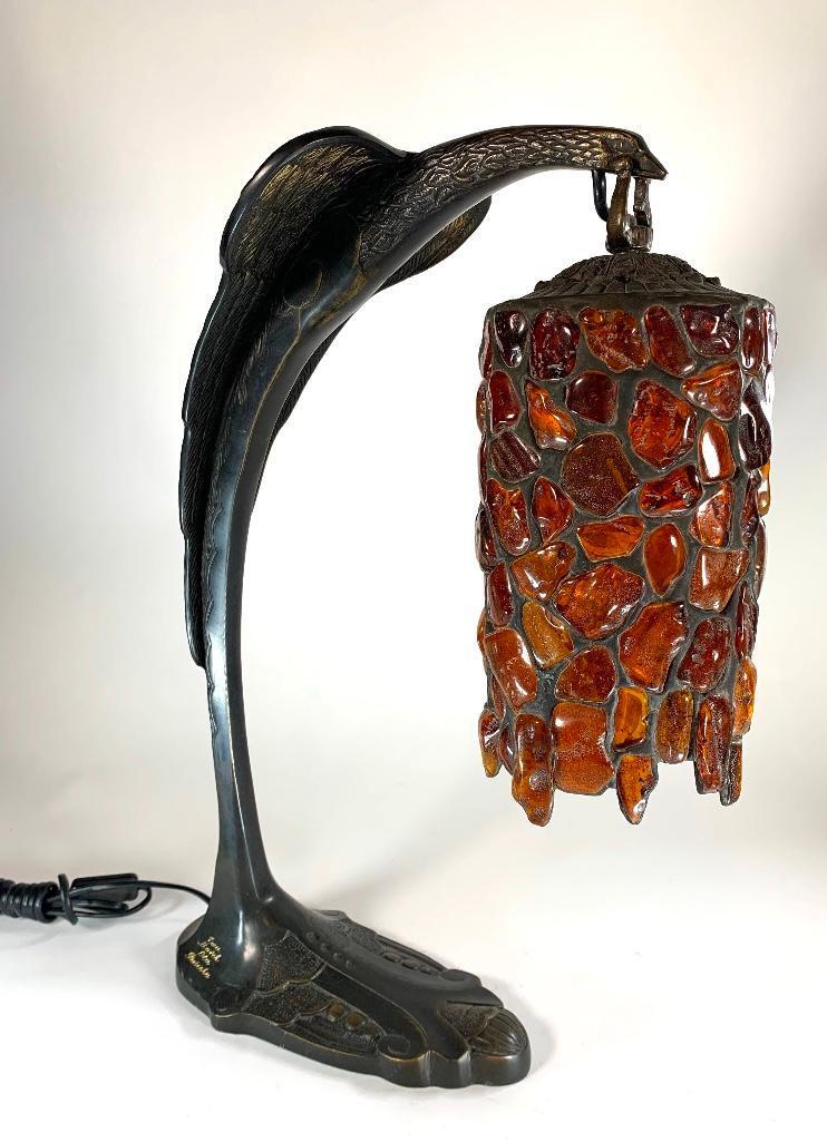Art Deco Style Bronze Lamp with Amber Shade: Art Deco Style Bronze Lamp with Amber Shade, the base castin the form of a stylized eagle, its beak supporting a pendant shade arranged with amber chunks. Base inscribed. 18.5 in.h. x 16 in. d. Condit