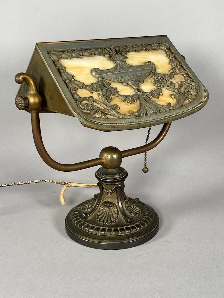 Bradley & Hubbard Slag Glass Desk Lamp: Slag Glass Desk Lamp, triangular shaped shade with rounded ends in caramel colored slag glass overlaid with a cast metal urn and bellflower swag, the base cast with drapery swags and scallop shells. S