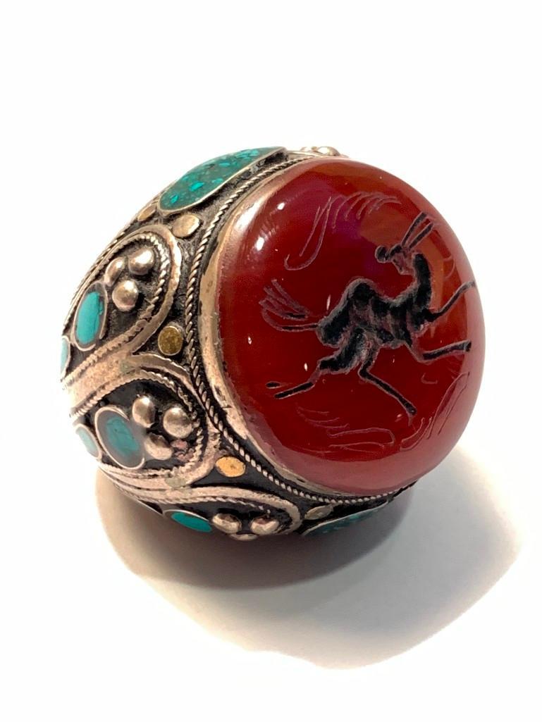 Tibetan Intaglio Carved Gentleman: Tibetan Intaglio Carved Gentleman's Ring, very overscale in size, in silver, carnelian and turquoise, the top with an intaglio carved stag over a design of lobed silver and turquoise. Dimensions: Ring