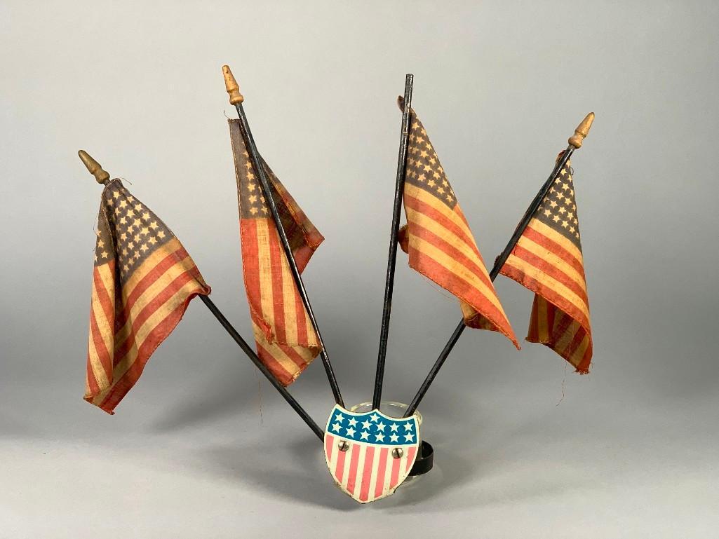 Vintage Radiator Cap Tin Shield Mascot: Vintage Radiator Cap Tin Shield Mascot, lithographed tin shield supporting 4 small vintage flags. Dimensions: 11.5 x 13 x 4.5 in. Condition: Effects of aging, tin shield dented, losses.