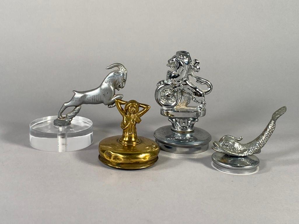 Three Vintage Automotive Mascots: Three Vintage Automotive Mascots, comprising NAF Lion in chrome, Dolphin, Jumping Goat and Partially Clothed woman with hands to head in brass. Dimensions: Lion 5 in. h. Goat, 4.5 in. h. Condition: Go