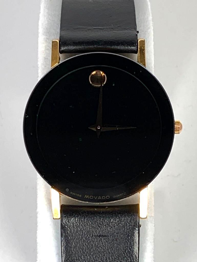 Movado Wrist Watch: Quartz movement, with black mirror finish dial, round gold tone marker, gold tone case and lugs, original Movado black leather strap with gold tone buckle. Dial 1-3/16 in. D, strap apprx 8"L. Conditio