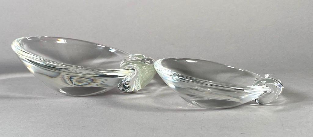 Two Steuben Crystal Bowls: Two Steuben Crystal Bowls, larger and smaller tilt bowls on off center bases, each applied at the rim with a wrap knop handle. Incised Steuben signature to each. With one original Steuben felt bag. Di