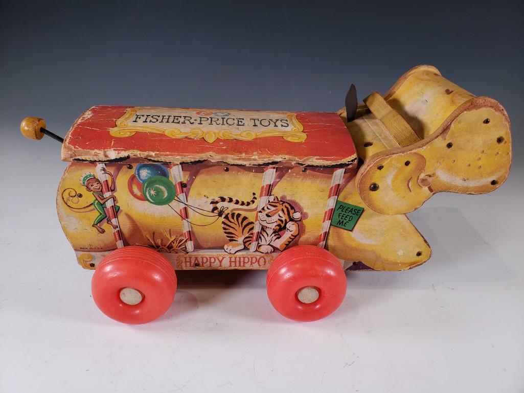 Fisher Price Lithographed Paper and Wood Happy Hippo: Fisher Price Lithographed Paper and Wood Happy Hippo, articulated pull toy on red plastic wheels. Dimensions: 7.5 x 15 x 7 in. Condition: As is with wear and loss to surfaces.