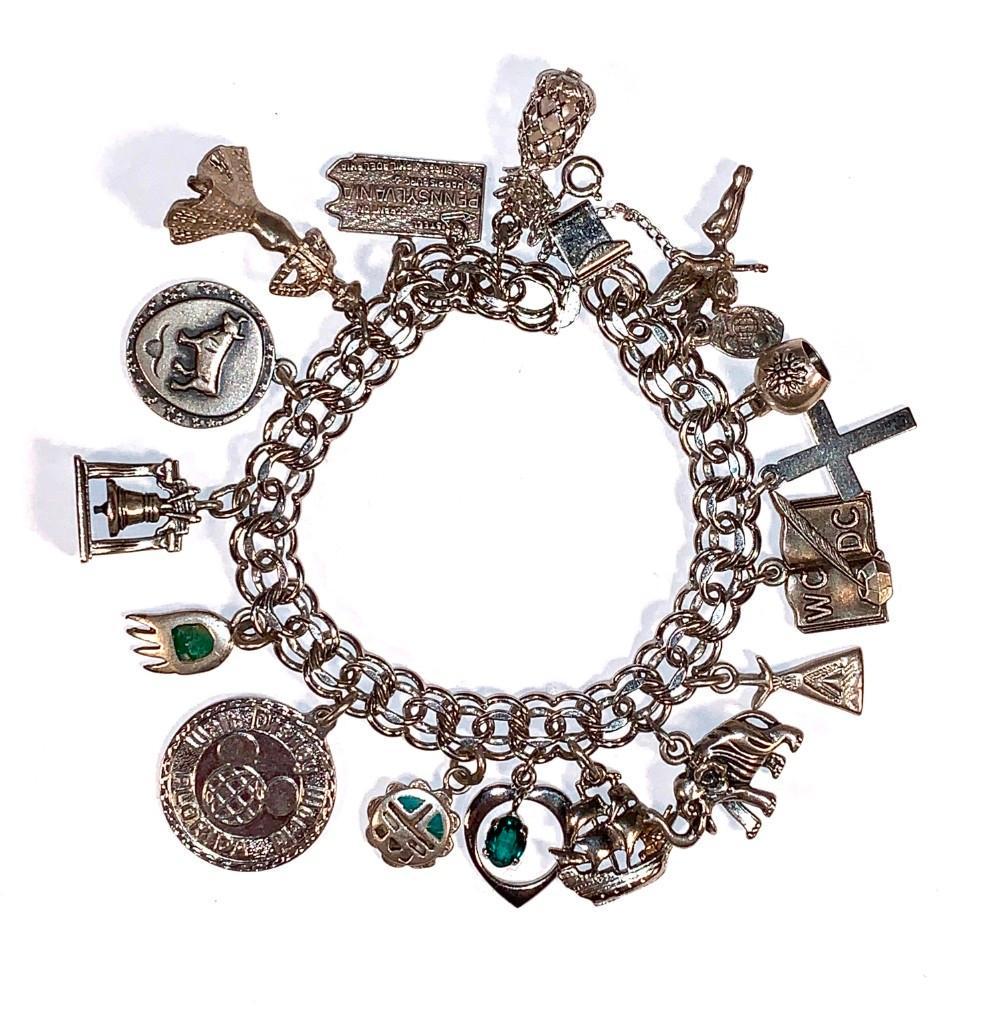Sterling Silver Charm Bracelet: Sterling silver link bracelet with seventeen charms, a few being an elephant, cross, Walt Disney World Florida, bear paw, Liberty Bell, and Pennsylvania State charm. Condition: very good.