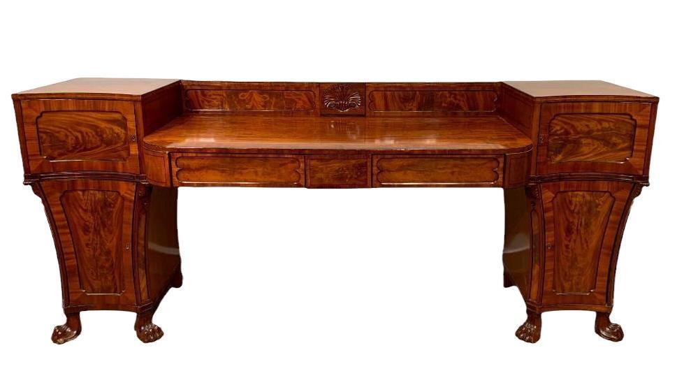 English Regency Flame Mahogany Sideboard, 19th c.: English Regency Flame Mahogany Sideboard, c. 1830-50, molded backsplash centered by a carved scallop shell motif, centering the rounded rectangular top with two drawers, supported by a pair of shaped 