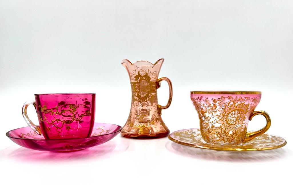 Two Moser Teacups and Saucers and Cream Jug: Two Moser Teacups and Saucers and Cream Jug, c.1890, each enameled with gilded foliate and floral scrolls. Dimensions:Cream jug 4.5 in.h. Condition: Very good with wear to gilding.