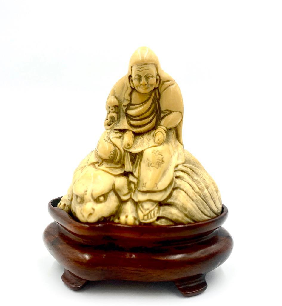 Chinese Antique Carved Bone Sculpture: Chinese Antique Carved Bone Sculpture features a Buddhist Disciple studying a sutra while seated on a lion. Lions are protectors in the Buddhist faith. The sculpture is intricately carved, even descri