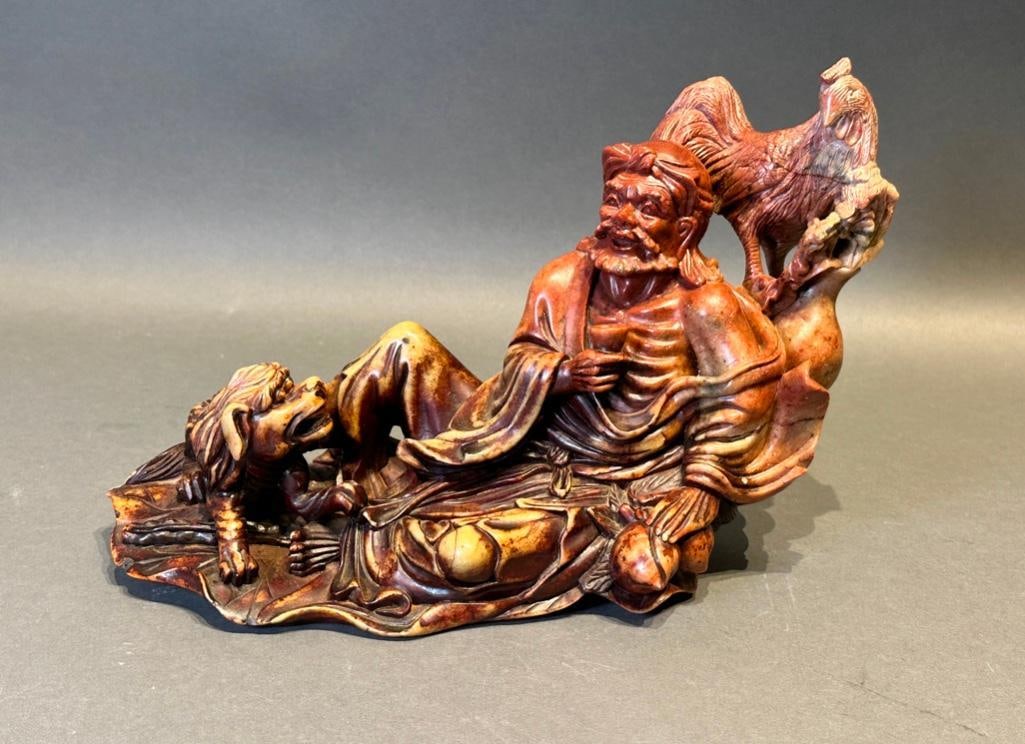 Chinese Hardstone Sculpture of Traveler: Chinese Hardstone Sculpture of Traveler, 20th century in date, depicts a man enjoying wine from a cup. He is accompanied by a Rooster perched on the tree above him and a lion at his feet. The stone va