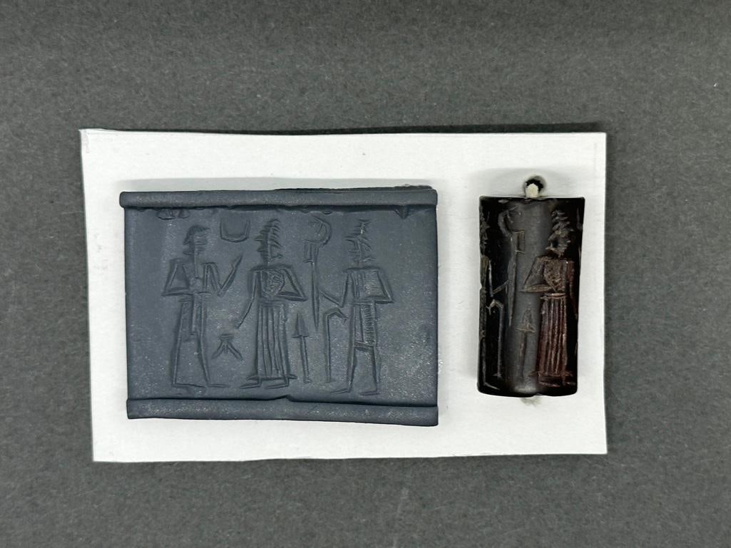 Old Babylonian Cylinder Seal, ca. 1800-1600 BCE: Old Babylonian Cylinder Seal, ca. 1800-1600 BCE, Carved seal of hematite, apprx 25.5 x 13.5mm. Three standing figures compose the scene. In the middle is a god in a horned tiara and long robe falling