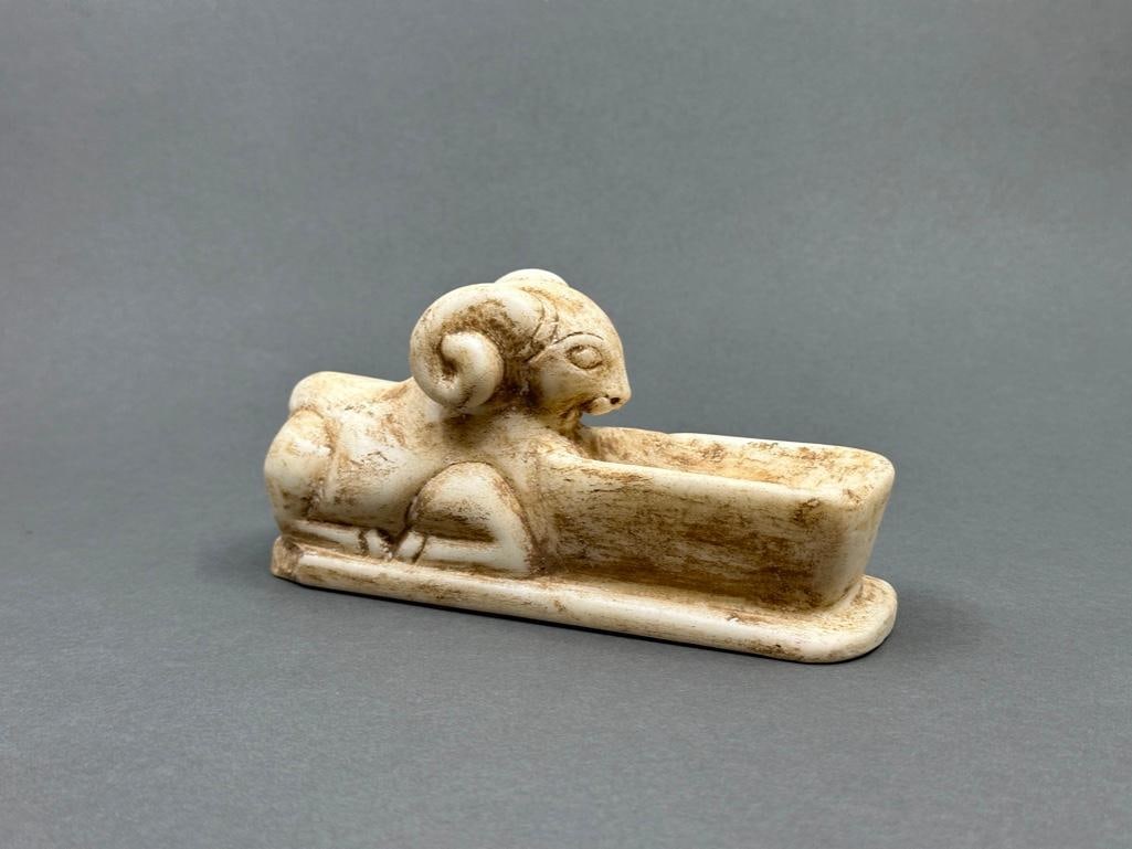 Carved Alabaster Ram Statuette: Carved alabaster recumbent ram in front of an elongated basin, raised on small foot. Apprx 3" x 6" x 2". From the collection of Juliane and Philip Lynch, Shaker Heights, Ohio. Condition: dirt through