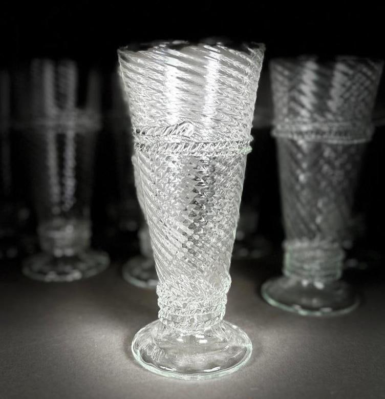 Eleven Juliska Style Hand Blown Flute Glasses: Eleven Juliska Style Hand Blown Flute Glasses, of conical tapering swirl form with applied notched bands around the form, on circular foot. Incised signature to base. Dimensions: 6.5 in. h. Condition: