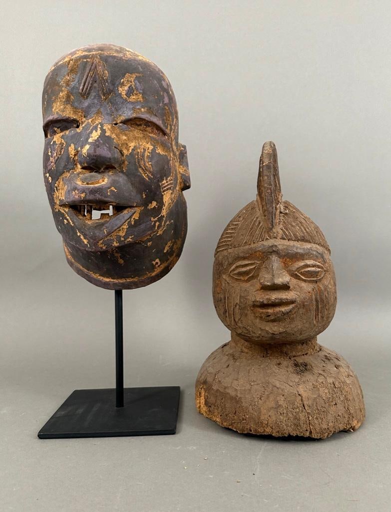 Two African Masks: Two African Masks, comprising a pigmented Makonde mask with facial scarification and open mouth showing teeth, together with a Yoruba mask carved with headdress. Makonde mask with metal base. Dimensio