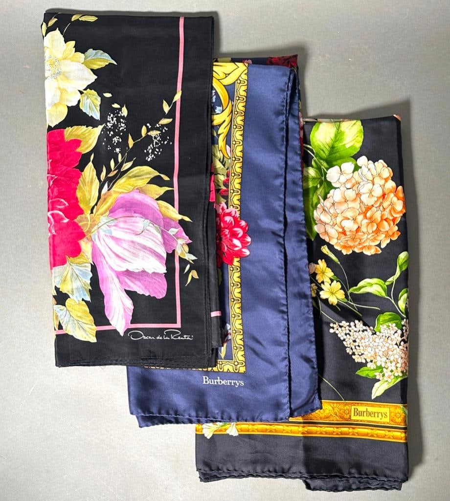 Three Silk Twill Scarves, Burberry and Oscar De La Renta: Three Silk Twill Scarves, Burberry and Oscar De La Renta, comprising a Burberry scarf with spring and summer flowers on a black ground, a Burberry scarf with red blue and pink flowers in gold scrolls