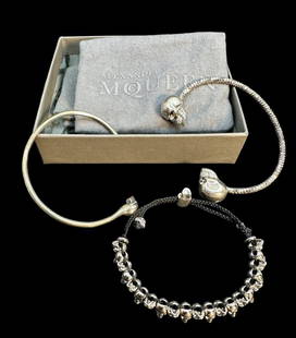 Three Alexander McQueen Skull Bracelets: Three Alexander McQueen Skull Bracelets, two open cuffs in silver plate or silver tone, together with a woven adjustable cord bracelet with multiple small skulls. Unmarked. In McQueen box with two dus