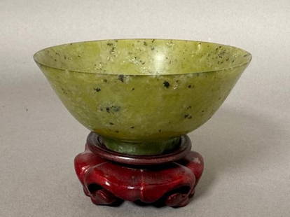 Small Chinese Jade Bowl: Small Chinese Jade Bowl, footed circular form in mottled medium green jade. On carved stand. Dimensions: 1.75 in.h. x 3 7/8 in. dia.Condition: Some fissures or hairlines near rim.