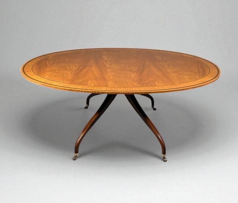 Baker Furniture Regency Style Oval Top Dining Table: Baker Furniture Regency Style Oval Top Dining Table, light toned mahogany top with nicely figured wood, with wide satinwood banded border, raised on four downswept legs and casters. Dimensions: 29 x 7